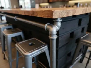 Industrial Chic Block Bar Table - High industrial-style bar table made from black-painted cinder blocks and metal piping, with a distressed wood top, surrounded by metal stools, close-up view