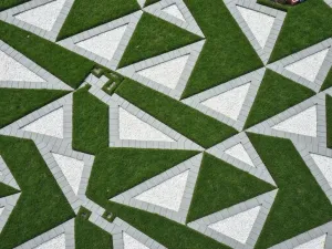 Geometric Pattern Path - Aerial view of a geometric path with alternating concrete and artificial grass triangles, creating a dynamic pattern, surrounded by white gravel