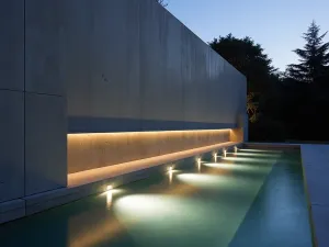 Modern Channel Wall - Minimalist concrete wall with horizontal channels creating sheets of water, lit dramatically from below at twilight