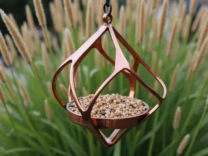 Modern Geometric Feeder - Contemporary geometric metal bird feeder in copper finish, minimalist design, positioned among ornamental grasses, aerial view of feeding platform