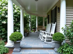 Classic Colonial Front Patio - Traditional small front patio with bluestone pavers, white columns, classic rocking chairs, symmetrical boxwood planters, and climbing hydrangea