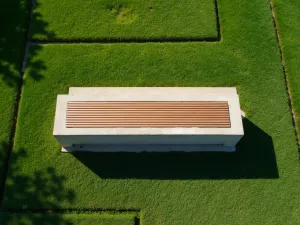 Modernist Concrete Bench Setting - Aerial shot of minimalist concrete bench with wooden seat on structured grass layout, geometric garden design, harsh midday shadows