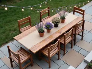 Rustic Teak Dining Setup - An aerial view of a weathered teak dining table with matching chairs, set against natural stone pavers, decorated with a burlap table runner and potted lavender centerpieces, surrounded by string lights overhead