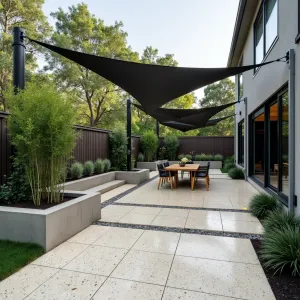 Terrazzo Modern Mix - Contemporary stamped concrete patio featuring a custom terrazzo-inspired pattern with embedded glass aggregate. Built-in concrete planters showcase black bamboo and Japanese forest grass, while angular steel shade sails provide modern shelter