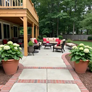 Traditional Comfort - Brushed concrete patio with brick border under a traditional wood deck. Classic outdoor furniture with red and beige cushions, wrought iron accents. Clay planters with Hydrangeas and Boxwood creating traditional appeal