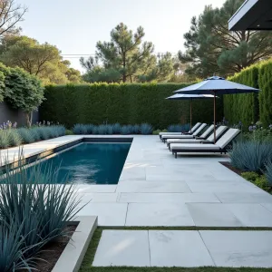 Contemporary Concrete Pool Deck - A smooth-finished concrete patio surrounding a modern pool, with oversized concrete pavers creating a striking pattern. Steel blue decorative grasses and architectural succulents in rectangular planters. Sleek lounge chairs and umbrellas.